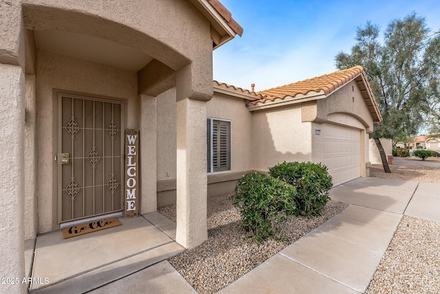 property entrance with a tile roof, an attached garage, driveway, and stucco siding