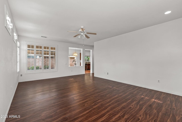 empty room with visible vents, a ceiling fan, dark wood-style flooring, and baseboards