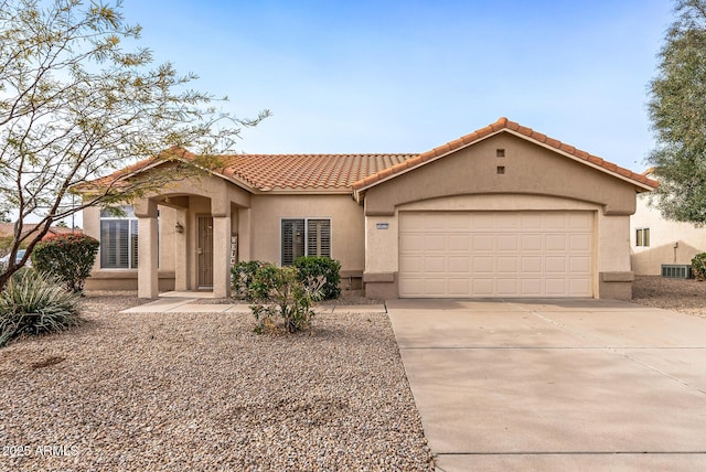 mediterranean / spanish-style house with central air condition unit, concrete driveway, a tile roof, stucco siding, and an attached garage