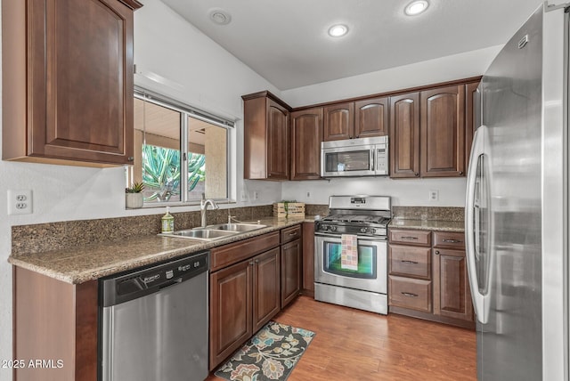 kitchen with light wood-type flooring, a sink, dark stone countertops, recessed lighting, and appliances with stainless steel finishes