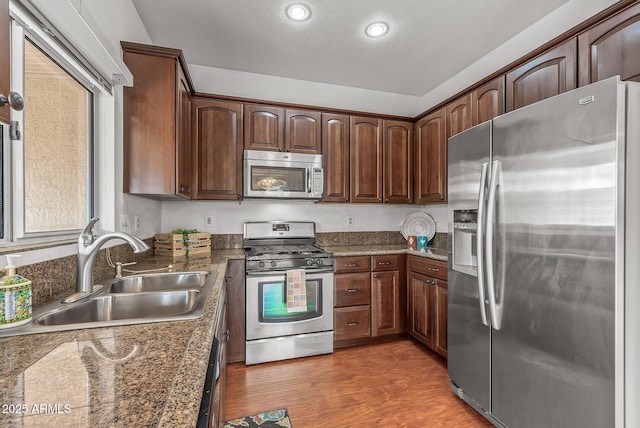 kitchen with a sink, dark stone counters, light wood finished floors, and stainless steel appliances