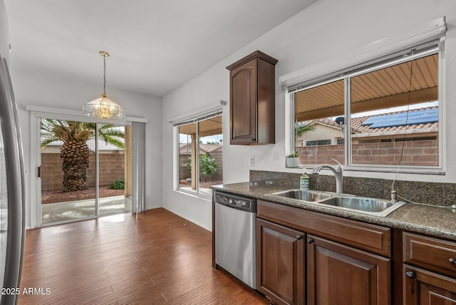 kitchen featuring dark countertops, dark wood-type flooring, stainless steel dishwasher, hanging light fixtures, and a sink