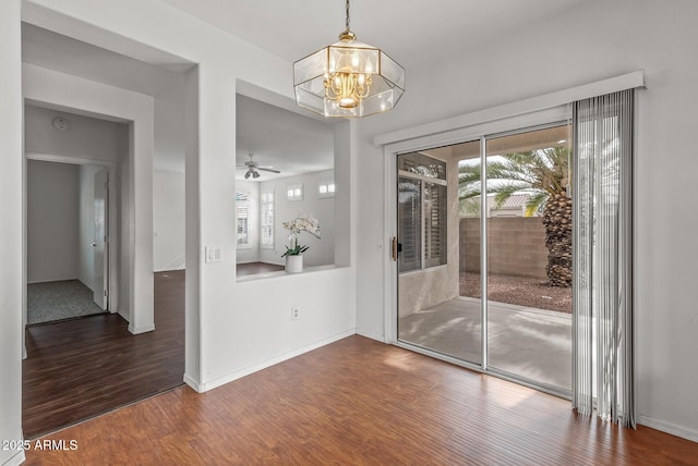 spare room with ceiling fan with notable chandelier, baseboards, and wood finished floors