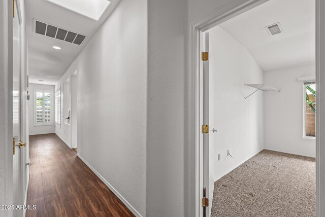 hall featuring a skylight, dark wood-style floors, visible vents, and baseboards