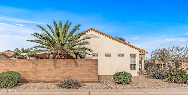 view of side of property featuring a tiled roof, fence, and stucco siding