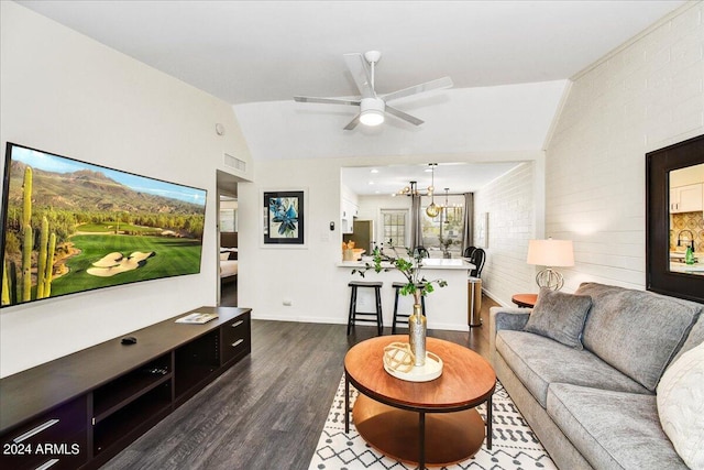 living room featuring lofted ceiling, ceiling fan with notable chandelier, dark wood-type flooring, and brick wall