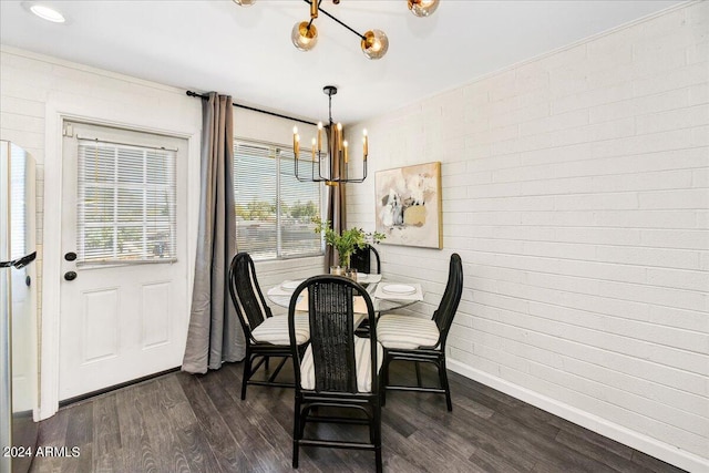 dining area with brick wall, dark wood-type flooring, and a notable chandelier