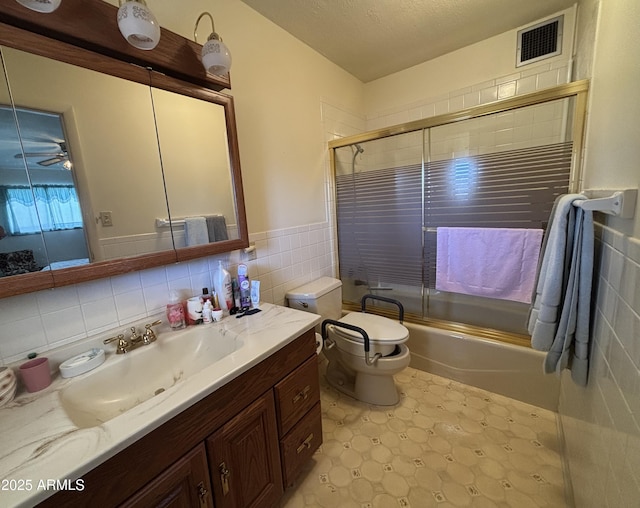 bathroom with visible vents, toilet, combined bath / shower with glass door, vanity, and tile walls