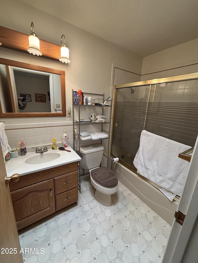 bathroom with toilet, enclosed tub / shower combo, tile walls, and vanity