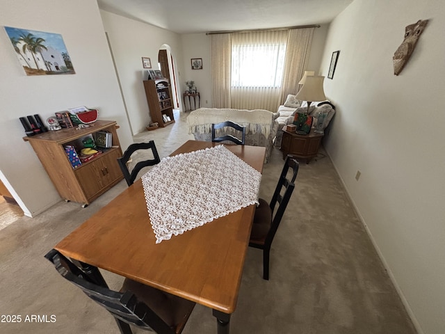 dining space with baseboards, arched walkways, and light colored carpet