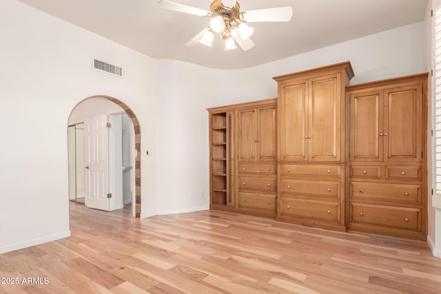 unfurnished bedroom with light wood-style floors, arched walkways, baseboards, and visible vents