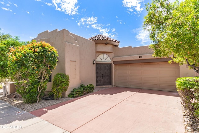pueblo revival-style home with an attached garage, driveway, a tile roof, and stucco siding