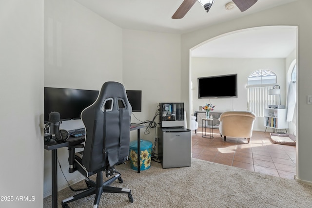 tiled home office with arched walkways, carpet flooring, and a ceiling fan