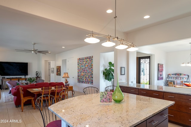 kitchen with ceiling fan, a center island, light stone counters, and hanging light fixtures