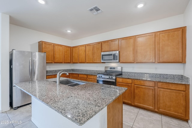 kitchen with visible vents, appliances with stainless steel finishes, brown cabinets, a kitchen island with sink, and a sink