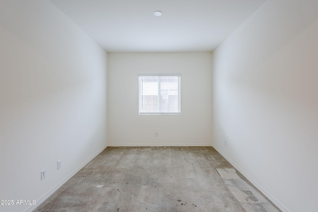 spare room featuring light colored carpet and baseboards