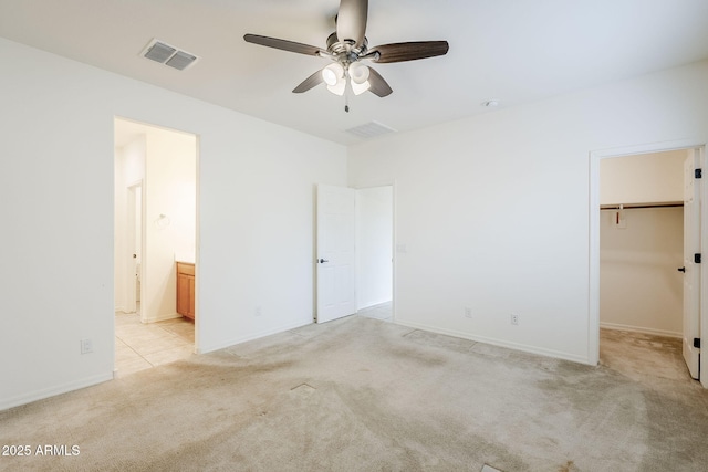 unfurnished bedroom with a spacious closet, connected bathroom, visible vents, and light colored carpet