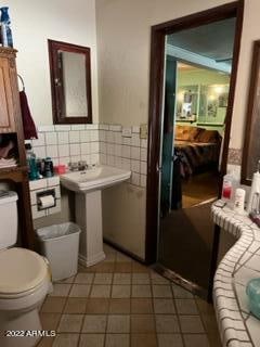 bathroom with backsplash, tile floors, toilet, and tile walls