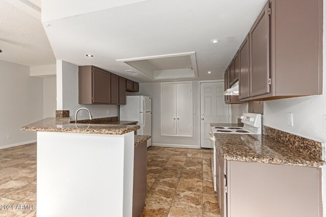 kitchen with kitchen peninsula, sink, white appliances, and dark stone countertops