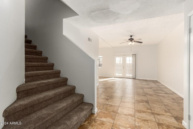 stairway featuring a textured ceiling, french doors, tile patterned flooring, and ceiling fan