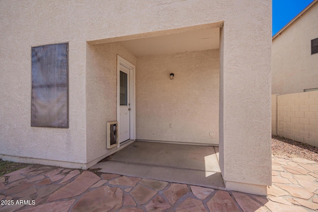 entrance to property featuring stucco siding, fence, and a patio area