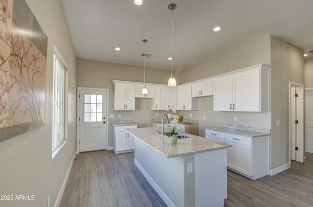 kitchen with white cabinetry, light stone countertops, sink, and an island with sink