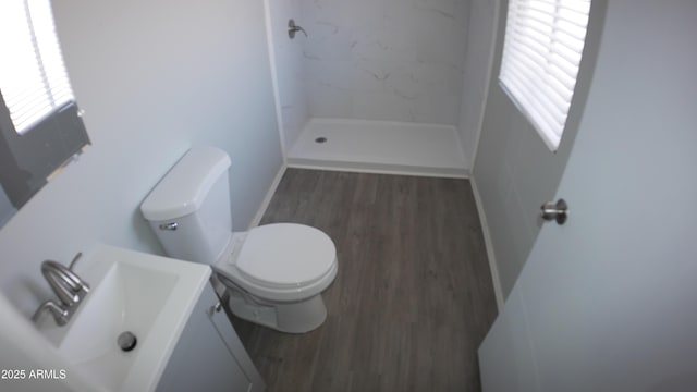 bathroom with a tile shower, vanity, hardwood / wood-style flooring, and toilet