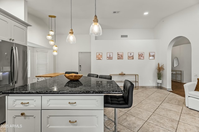 kitchen featuring dark stone counters, a kitchen breakfast bar, hanging light fixtures, light tile patterned floors, and stainless steel fridge with ice dispenser