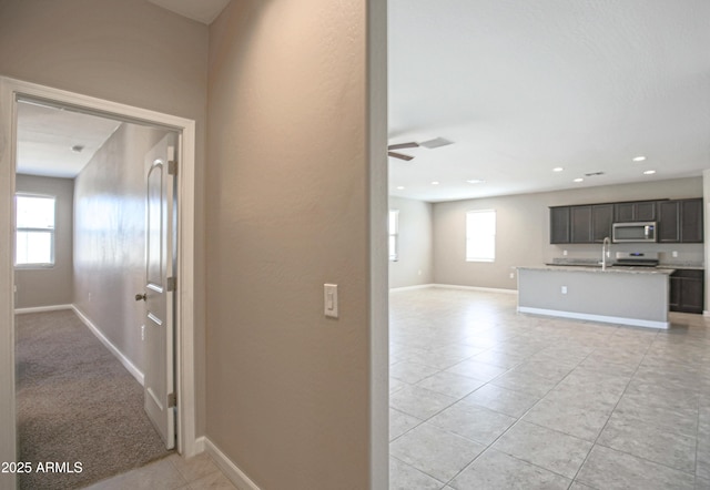 hallway featuring recessed lighting, a sink, baseboards, and light tile patterned floors