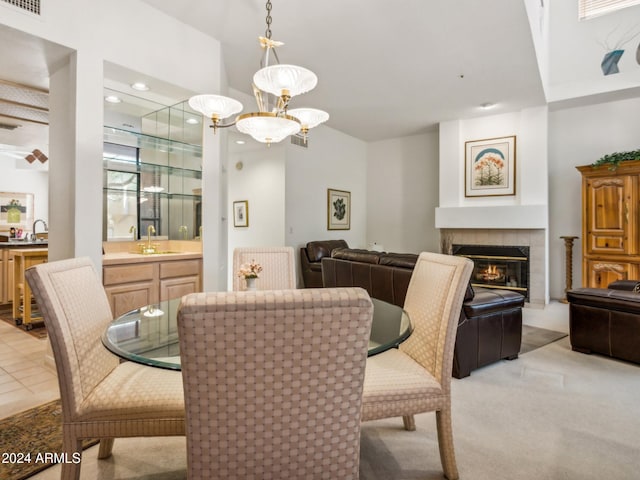 dining room featuring a tiled fireplace, light carpet, sink, and a notable chandelier