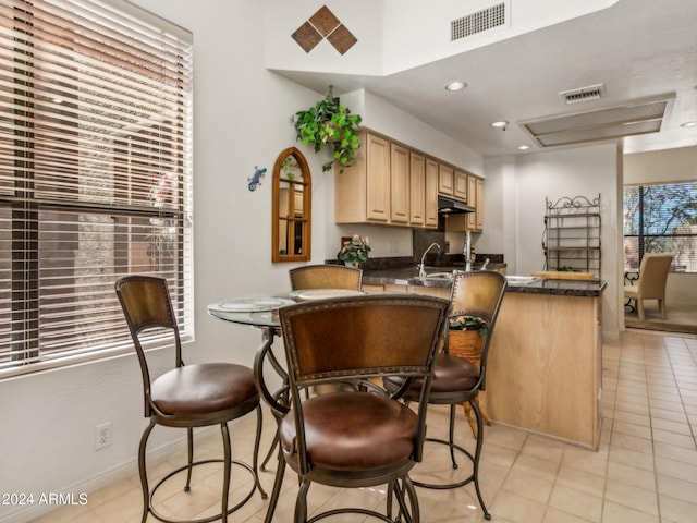 kitchen with light brown cabinets, light tile patterned flooring, kitchen peninsula, and sink