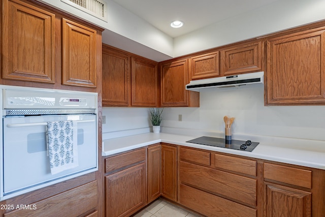 kitchen featuring oven, black electric cooktop, and light tile patterned flooring