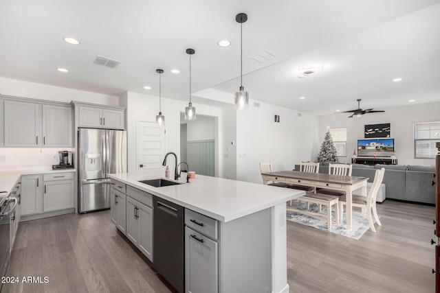 kitchen featuring gray cabinetry, ceiling fan, decorative light fixtures, a center island with sink, and appliances with stainless steel finishes