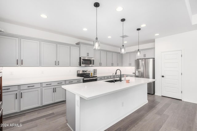 kitchen featuring hardwood / wood-style floors, decorative light fixtures, gray cabinets, a kitchen island with sink, and appliances with stainless steel finishes