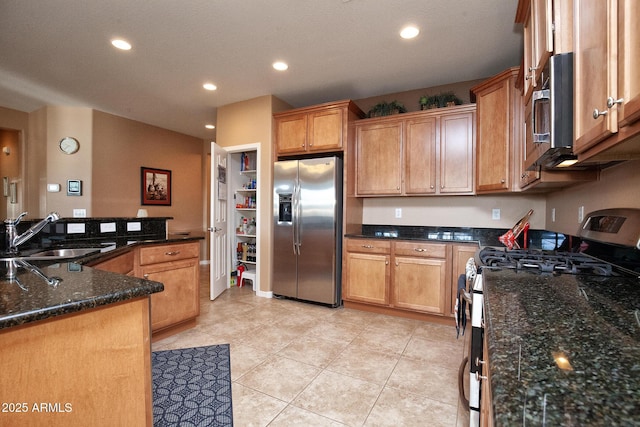 kitchen with stainless steel appliances, light tile patterned flooring, sink, and dark stone countertops