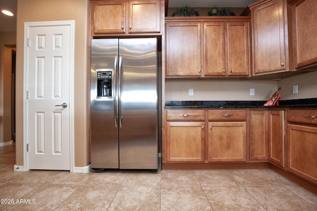 kitchen featuring dark stone countertops, light tile patterned floors, and stainless steel fridge