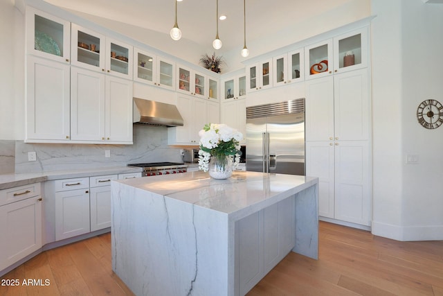 kitchen with light stone countertops, stainless steel appliances, white cabinetry, and wall chimney exhaust hood