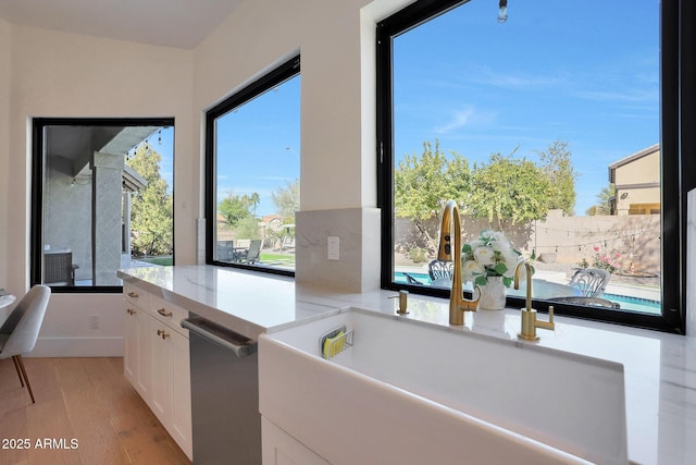 kitchen with light stone countertops, white cabinetry, stainless steel dishwasher, sink, and light wood-type flooring