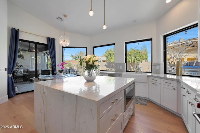 kitchen featuring light stone counters, hanging light fixtures, white cabinets, and stainless steel microwave