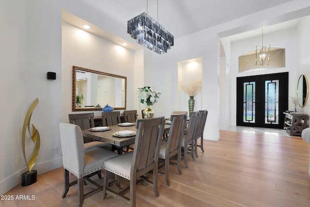 dining area with light hardwood / wood-style floors, a notable chandelier, and french doors