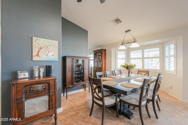 dining area with light tile patterned floors, baseboards, visible vents, a textured wall, and lofted ceiling