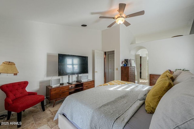 bedroom featuring lofted ceiling, stone finish floor, arched walkways, and a ceiling fan