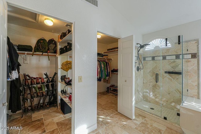 bathroom featuring a spacious closet, a stall shower, visible vents, and stone tile floors