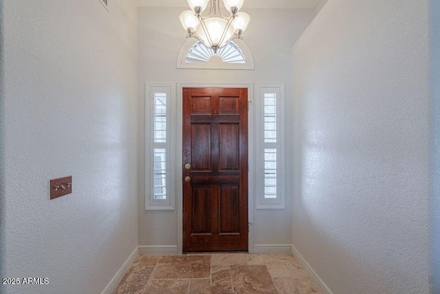 entryway with stone finish floor, a notable chandelier, and baseboards