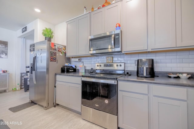 kitchen featuring dark countertops, light wood-type flooring, recessed lighting, appliances with stainless steel finishes, and backsplash