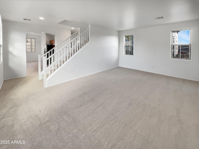 unfurnished living room with stairway, carpet, visible vents, plenty of natural light, and arched walkways