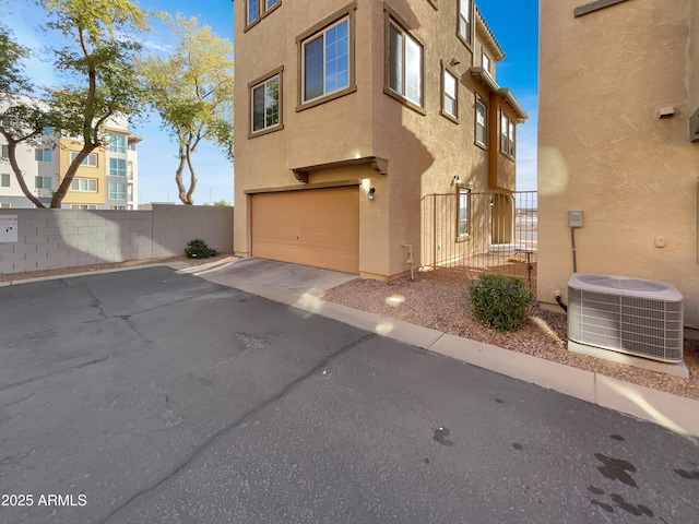 view of home's exterior with fence, driveway, central AC, stucco siding, and a garage