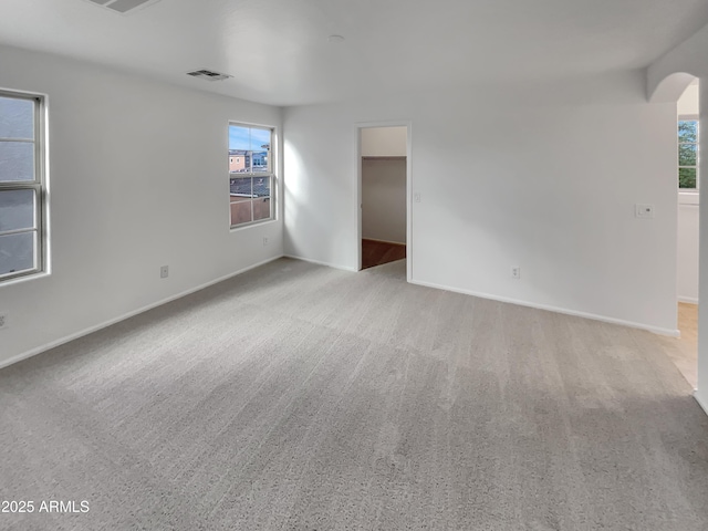 spare room featuring arched walkways, visible vents, light carpet, and baseboards