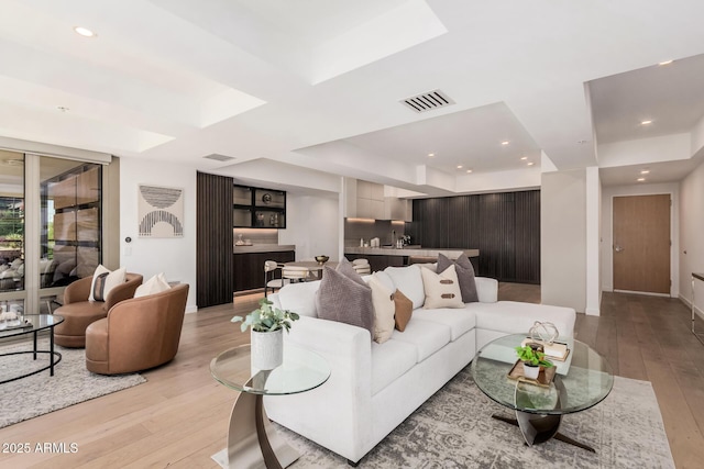 living room with a tray ceiling, light wood finished floors, recessed lighting, and baseboards