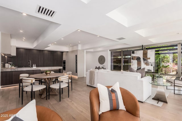 dining area featuring light wood-style floors, a tray ceiling, and a skylight